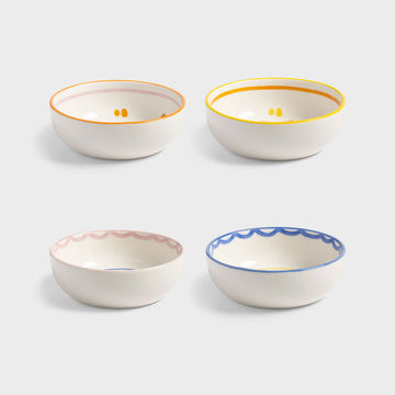 Top down view of four ceramic bowls with colourful sun designs on a light grey background.