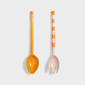 Two salad servers, one orange and one with a striped design, on a light gray background.