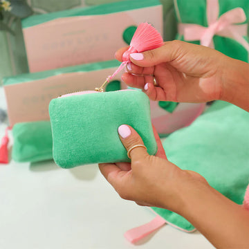 A velvet coin purse in green with a pink zipper and pink tassel. 