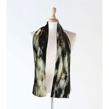 A silk scarf is worn draped over the shoulders of a mannequin. The scarf is printed with an abstract design in dark green and black.