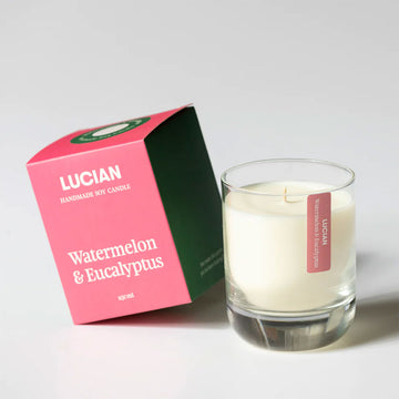 A glass candle next to a pink box with the text 'Lucian Watermelon & Eucalyptus'.