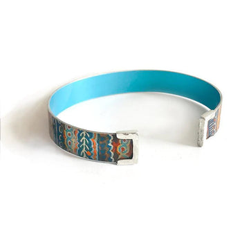A cuff bangle printed with artwork by Murdie Morris on the outside and plain blue on the inside.