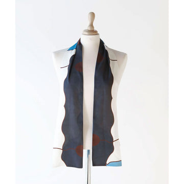A silk scarf is draped over the shoulders of a mannequin and printed with an abstract pattern in dark blue, red and white.