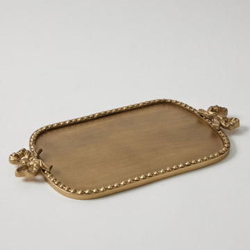 An antique gold tray with a bow on each end and round embossed circles around the edge.
