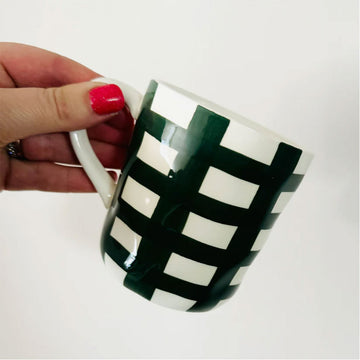 A hand is holding a white and emerald green hand painted mug.
