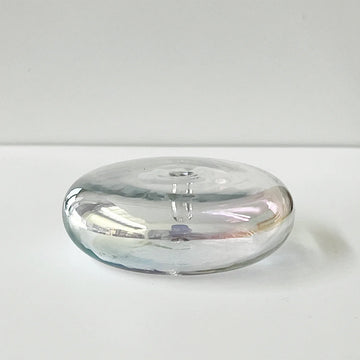 An iridescent round glass vessel on a white surface.