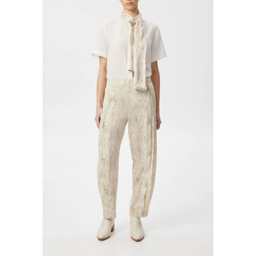 A model wears a silk scarf around her neck over a white top with pants that match the scarf.