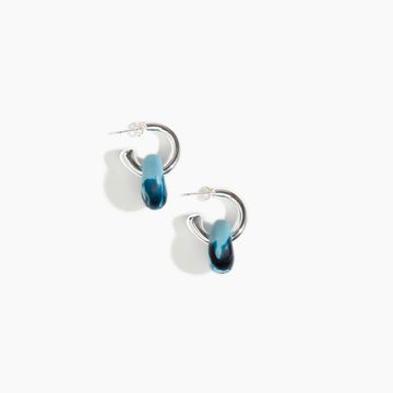 A pair of open hoop earrings in silver with a resin piece hanging off the hoop in blue.