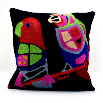 A wool cushion printed with two colourful birds on a black background in artwork by Karen Barnes.