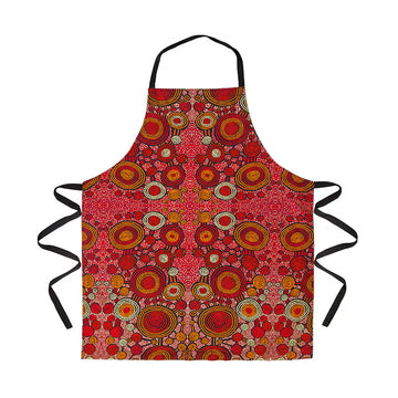 A cotton apron lying flat and printed with red and orange Indigenous artwork by Teddy Gibson.