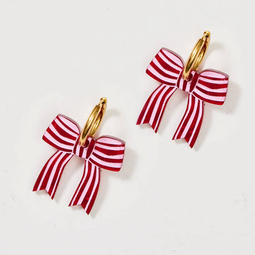 A pair of gold hoop earrings with red bows attached to the hoop.
