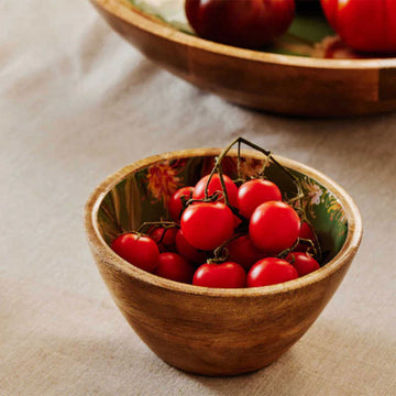 A small wooden bowl with flowers printed on the inside on a green background.