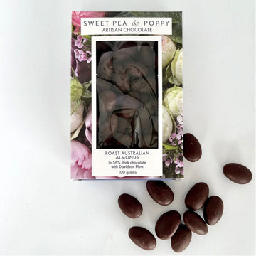 A packet with chocolate covered almonds inside with a floral border and clear window. There are a few loose almonds in front of the box.