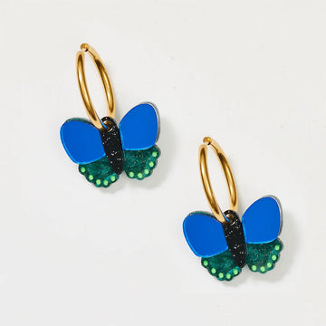 A pair of gold hoop earrings with cobalt and green butterflies attached to the hoops.