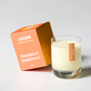 A glass candle next to an orange box with the text 'Lucian Mandarin & Sandalwood'.