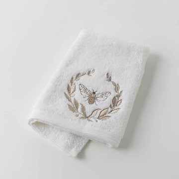 A folded over white hand towel embroidered with a bee and wreath motif.