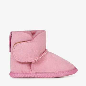 Side view of a baby sized ugg boot in pink with a velcro strap.