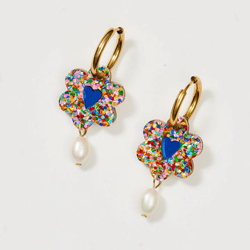 A pair of gold hoop earrings with a flower covered in rainbow glitter attached with a pearl at the bottom.