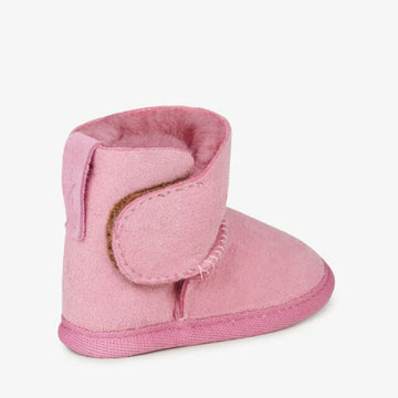 Side view of a baby sized ugg boot in pink with a velcro strap.