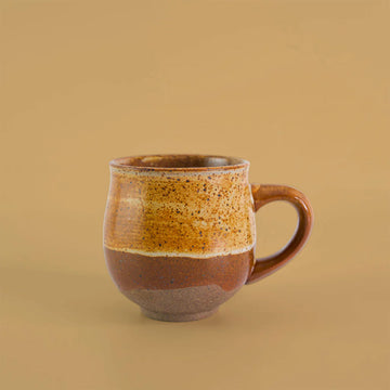 Ceramic mug with brown and beige speckled design on a beige background.