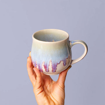 Hand holding a ceramic mug with a gradient design against a plain background.