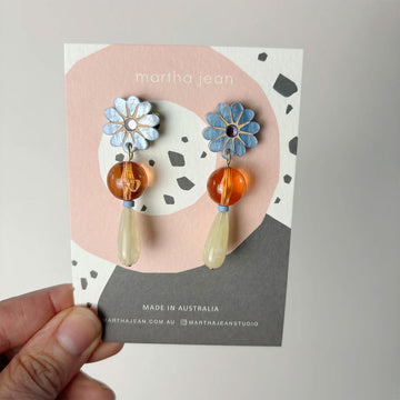 A pair of drop earrings in blue and orange with a flower at the top followed by a round bead and tear drop bead.