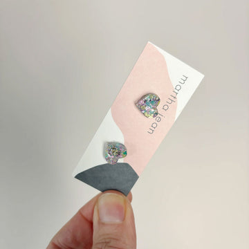 A pair of heart shaped stud earrings attached to a card made from pastel glitter.