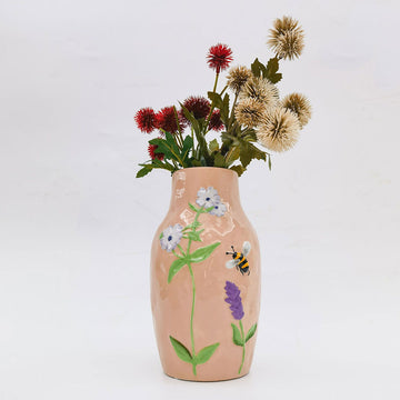 A ceramic light pink vase embossed with flowers and a bee.
