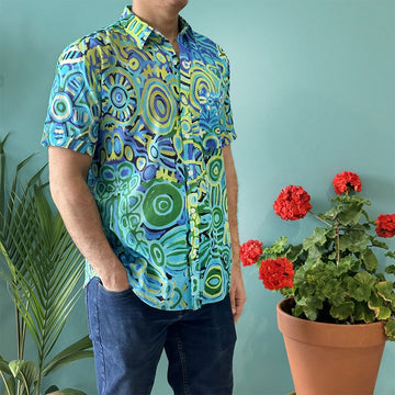 Front view of a model wearing a shirt printed with artwork by Cedric Varcoe in blue and green with jeans.