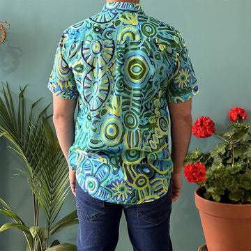 Front view of a model wearing a shirt printed with artwork by Cedric Varcoe in blue and green with jeans.