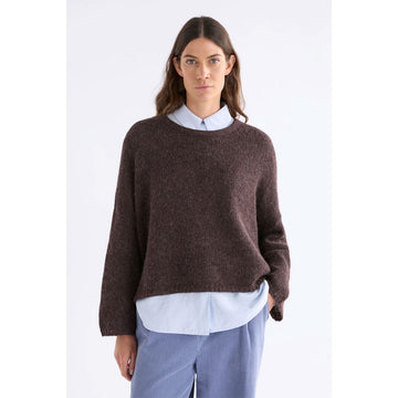 Front view of a model wearing a brown sweater over a shirt and blue pants.