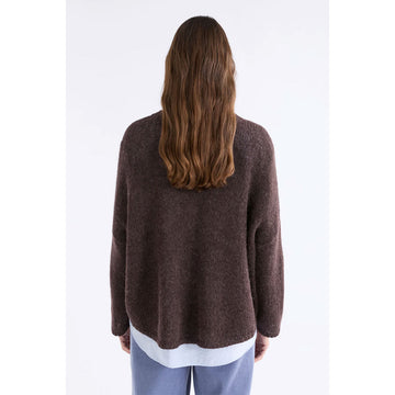 Front view of a model wearing a brown sweater over a shirt and blue pants.