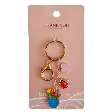 A gold keyring with charms hanging off it in the shape of a heart, ladybug and tulips in a pot.