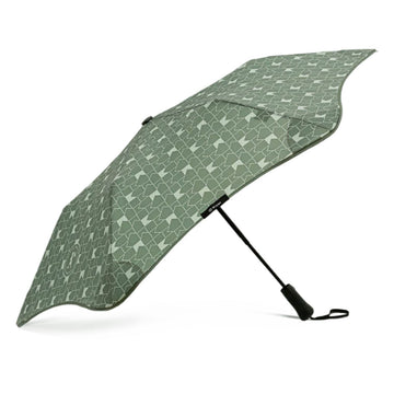 A green and white geometric patterned umbrella is standing open on its black handle.