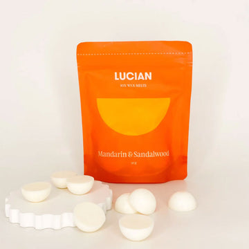 An orange packet with the text 'Lucian Mandarin & Sandalwood' with wax melts in front.