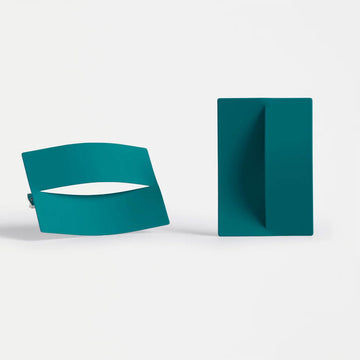 Two large teal-colored geometric earrings on a light gray background.