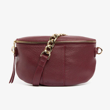 Front view of a burgundy bag with a gold zip around the top and half gold chain, half burgundy strap.