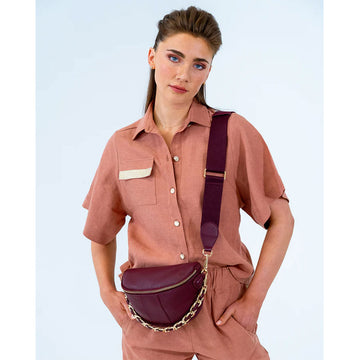 Front view of a burgundy bag with a gold zip around the top and half gold chain, half burgundy strap.