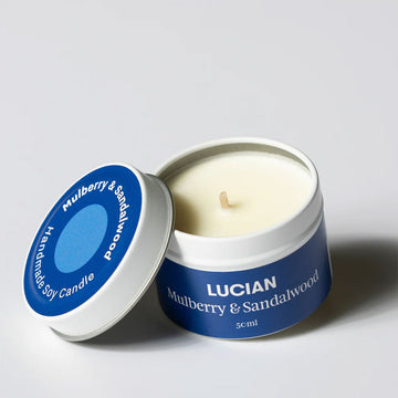 A small candle in a tin with the lid open. The lid and tin are covered with a blue label with the text 'Lucian Mulberry & Sandalwood'.