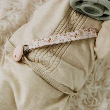 A dummy clip attached to a pink strap printed with gumnut babies by May Gibbs.