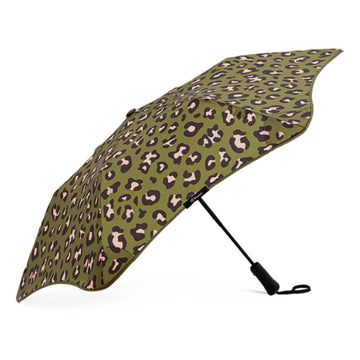 An open umbrella printed with leopard print on an olive green background is resting on its black handle.