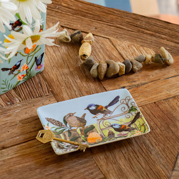 A ceramic trinket tray with a painting of birds on a fence and flowers.