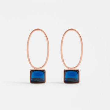 A pair of stud drop earrings with a hollow gold oval and a blue gem in a gold bezel below.