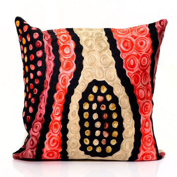 A square cushion embroidered with a red, black and cream coloured design.