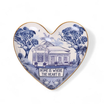 A heart shaped ceramic trinket dish illustrated with a house and trees with the text 'Home is Where the Heart Is'.