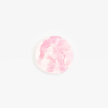 An irregular shaped round resin coaster in light pink.
