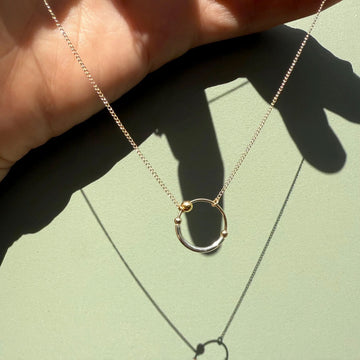 Gold necklace with a circular pendant held by a hand on a light green background