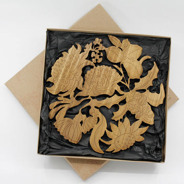 An open box with a wooden trivet inside shaped like flowers and linked together on black tissue paper.