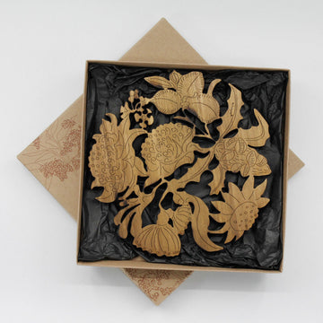 An open box with a wooden trivet inside shaped like flowers linked together on black tissue paper.