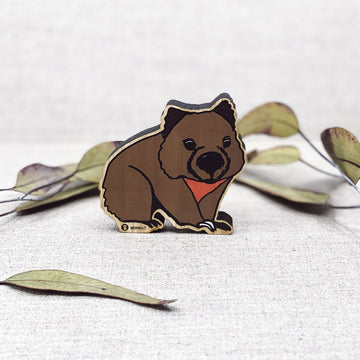 A wooden figurine shaped and painted like a wombat with gum leaves sitting behind.